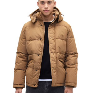 A person is wearing a tan puffer jacket with a hood, black shirt, and dark jeans.