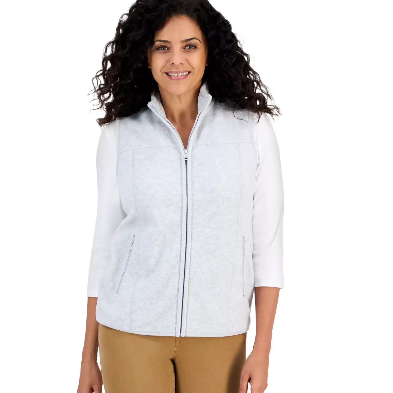 A woman is wearing a light gray zip-up fleece vest over a white long-sleeve top and tan pants.
