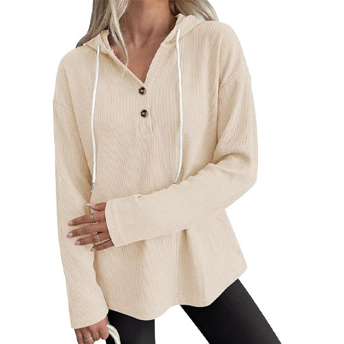 A woman wears a beige waffle-knit long-sleeve hoodie with a three-button placket and drawstrings, paired with black leggings.