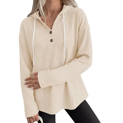 A woman wears a beige waffle-knit long-sleeve hoodie with a three-button placket and drawstrings, paired with black leggings.