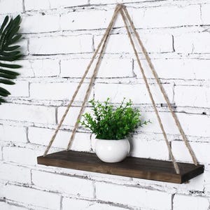 Two triangular rope-hung wooden shelves against a white brick wall, one with a potted plant.