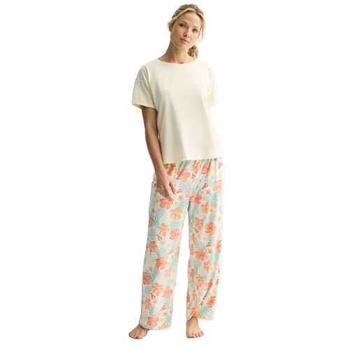 A woman wears a cream short-sleeve top paired with floral-patterned wide-leg pajama pants in pastel colors.
