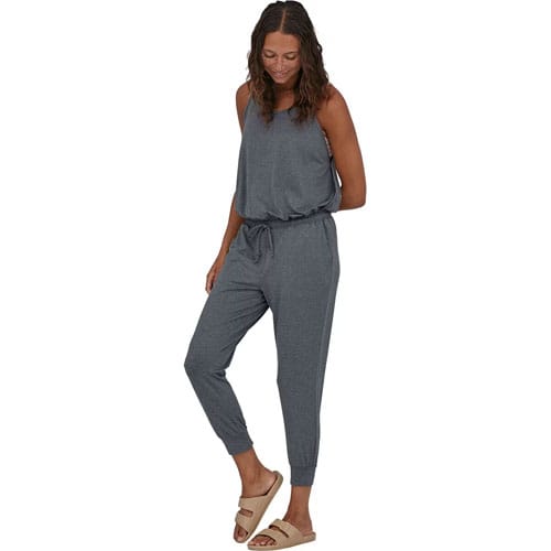 A woman is wearing a grey sleeveless jumpsuit with a drawstring waist and sandals.