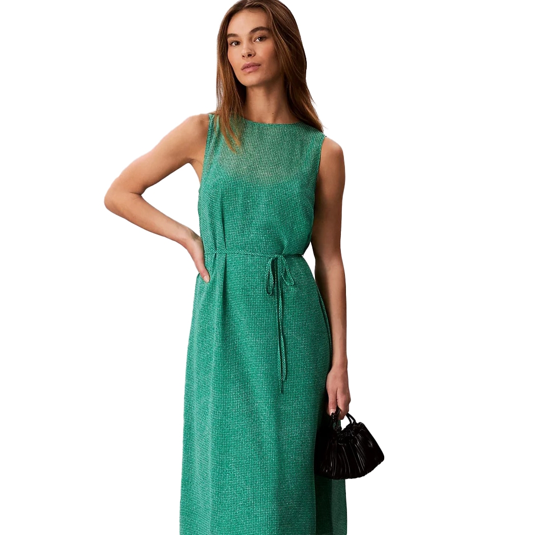 A woman is wearing a sleeveless green dress with a tie waist, paired with a small black handbag.