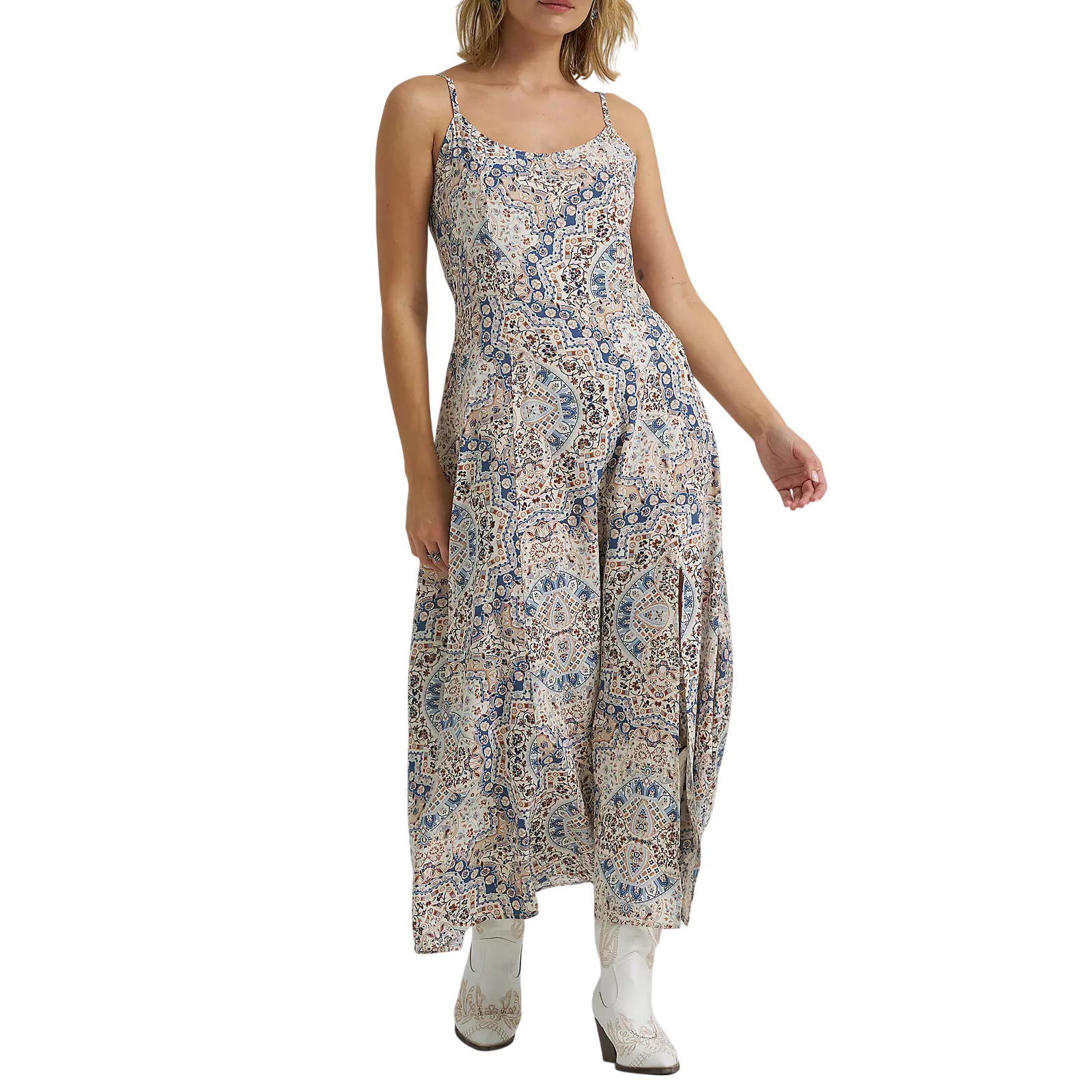 A woman in a patterned maxi dress, cowboy hat, and white cowboy boots.