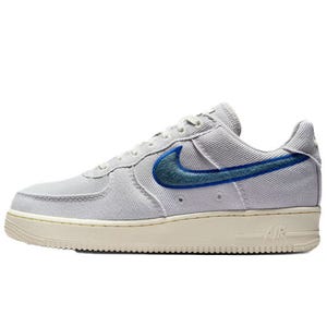 A light gray Nike Air Force 1 sneaker with a textured blue Swoosh logo on the side and a cream sole.