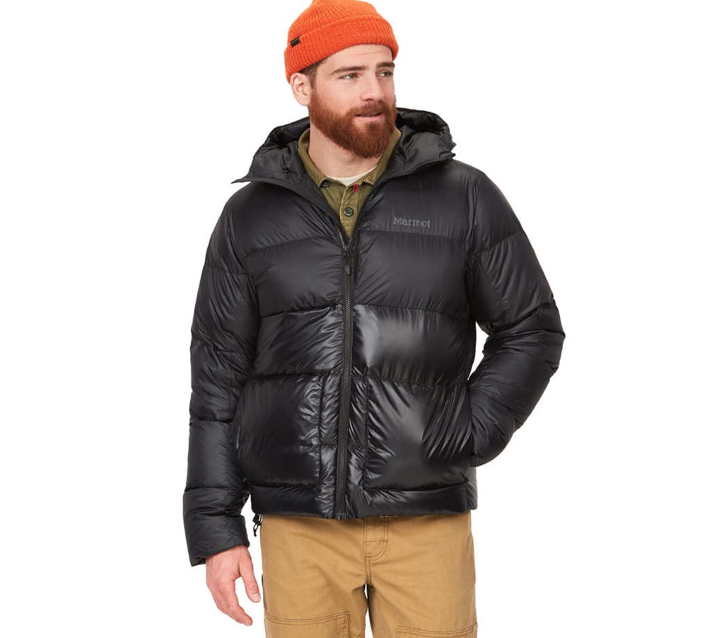 A person is wearing a black Marmot insulated puffer jacket, khaki pants, a green shirt, and an orange beanie.