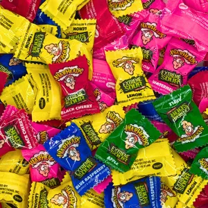 Warheads Extreme Sour candies in various flavors, including black cherry, lemon, blue raspberry, watermelon, and apple, are shown with colorful, individually wrapped packages.