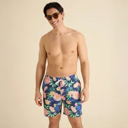 A man is wearing floral-patterned swim shorts with a navy background and elastic waistband, paired with round sunglasses.