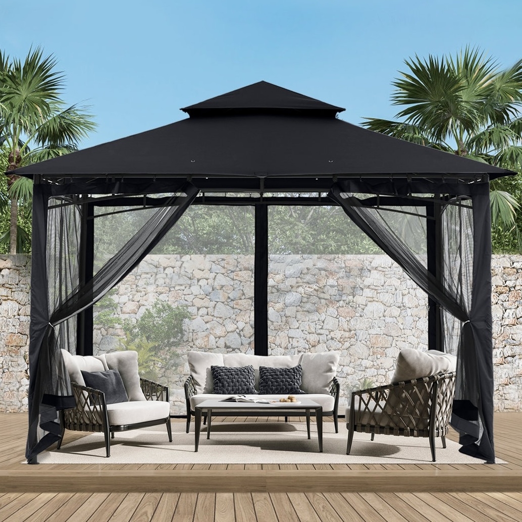 A black gazebo with sheer curtains surrounds a patio setup featuring a white coffee table and two cushioned chairs on a wooden deck, against a stone wall backdrop.