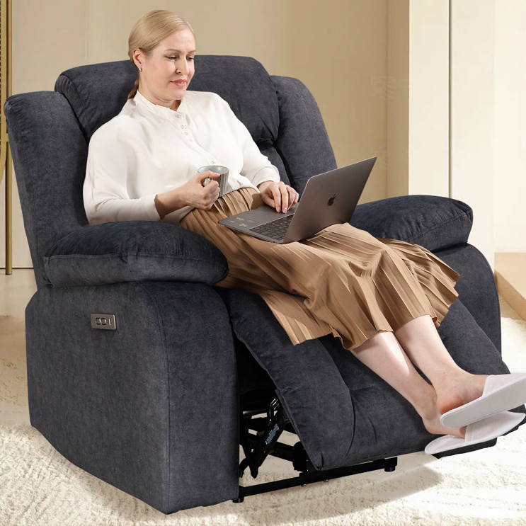 A person is sitting in a plush, gray power recliner with extended footrest, featuring USB ports on the side for device charging.