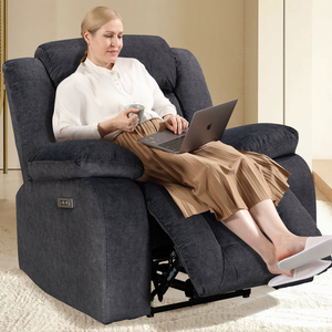 A person is sitting in a plush, gray power recliner with extended footrest, featuring USB ports on the side for device charging.