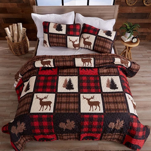 Quilt set featuring a checkered pattern with deer and tree designs in red, brown, and white, shown on a bed with matching pillows and a rustic decor setting.