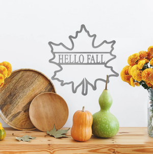 A wooden round plate, a small wood bowl, assorted gourds, maple leaves, and a vase of yellow flowers on a table, with a 'Hello Fall' leaf sign in the background.
