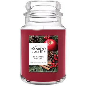 Yankee Candle jar with \“Red Apple Wreath\“ fragrance, featuring a holiday-themed label with an apple, cinnamon sticks, pine cones, and berries.