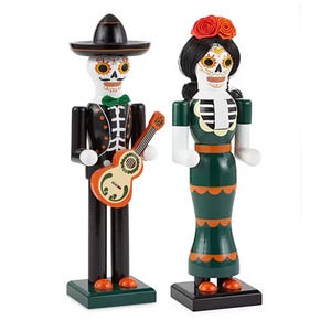 Two decorative figurines representing a male and a female skeleton dressed in traditional Mexican Day of the Dead attire, complete with painted skull faces and festive clothing.