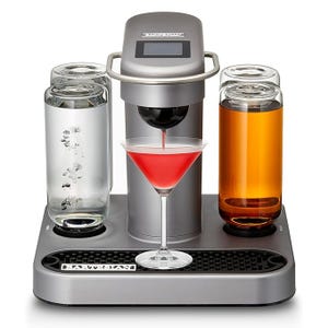 A countertop cocktail machine with three clear liquid containers and a central spout dispensing a red drink into a martini glass.