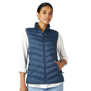 A woman is wearing a blue, quilted puffer vest over a white long-sleeve shirt, paired with light blue jeans.
