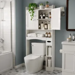A bathroom features a white over-the-toilet storage unit holding towels, bottles, and plants. The space includes a toilet, bathtub with shower, hexagonal floor tiles, and a blue wall with a white vanity.