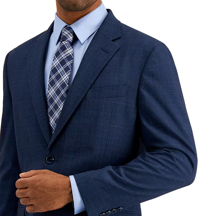 A man wearing a dark blue checkered suit with a light blue dress shirt and a plaid tie.