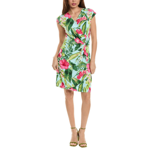 A woman is wearing a knee-length, short-sleeved dress with a vibrant tropical floral pattern in green, pink, and white, paired with green strappy sandals.