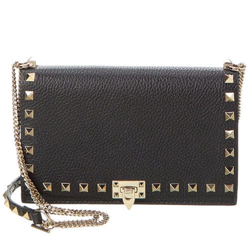 A black leather crossbody bag with gold pyramid studs, featuring a chain strap and a clasp closure on the front.