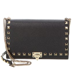 A black leather crossbody bag with gold pyramid studs, featuring a chain strap and a clasp closure on the front.