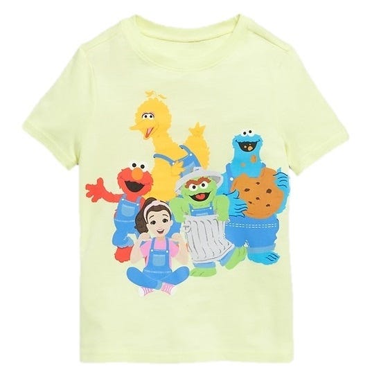 A light yellow t-shirt features popular children's characters including a yellow bird, a red puppet, a green character in a trash can, a blue cookie-loving creature, and a girl, all wearing overalls.