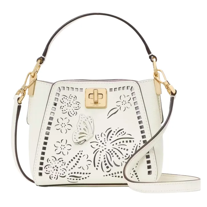 White handbag with floral and butterfly cutout designs, gold-tone hardware, and a top handle along with a detachable shoulder strap.