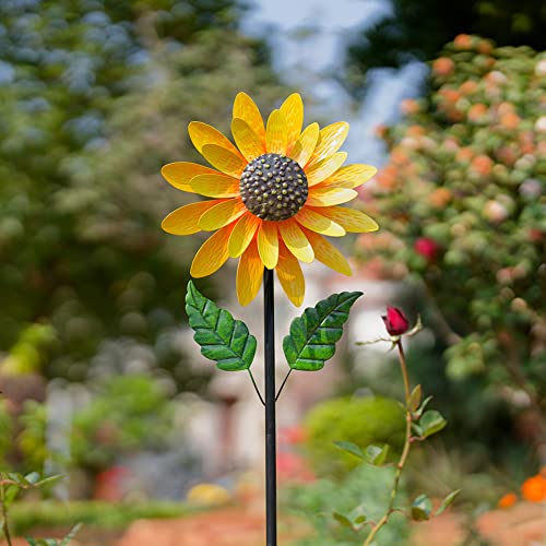 A decorative metal garden stake features a sunflower design with yellow petals and green leaves, set in an outdoor garden environment.