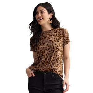 A woman wearing a brown polka-dot short-sleeve blouse, paired with black pants. She has long dark hair and is accessorized with hoop earrings.