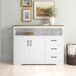 A white modern sideboard features two cabinet doors and three drawers beneath a wooden countertop, with decorative items and framed pictures above.