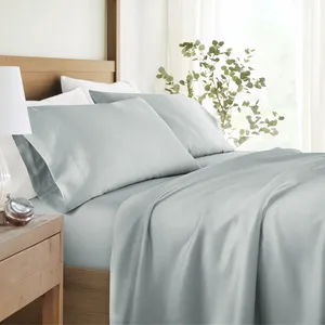 A neatly made bed featuring light gray silk sheets and pillowcases, set against a wooden headboard with a plant and a bedside table with a lamp and a clock.