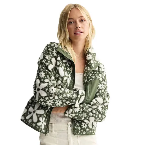 A woman wears a green and white fleece jacket with a floral pattern, paired with a white top and pants.