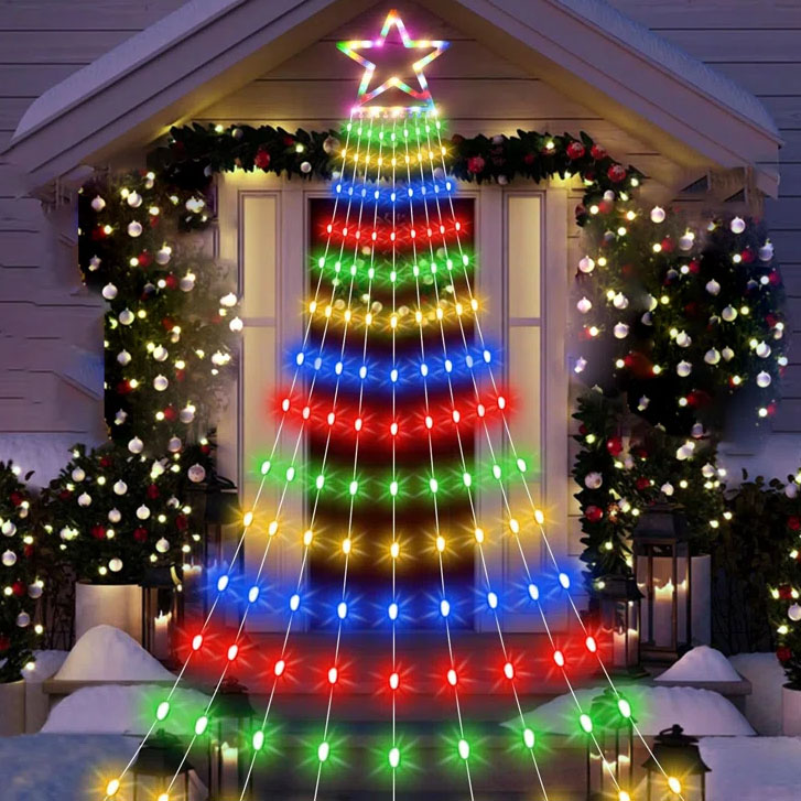 A cascade of multi-colored LED lights forms a Christmas tree shape with a star on top, flanked by garlands and snow-covered bushes.