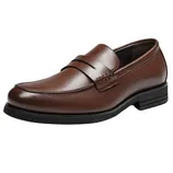 A brown leather loafer with a black sole, featuring a sleek design and a decorative strap across the top.