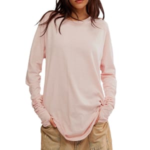 A woman is wearing a light pink long-sleeve shirt with a casual fit and tan pants with a paint-splatter design.