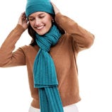 A woman is wearing a turquoise knit hat and matching scarf with a brown sweater.