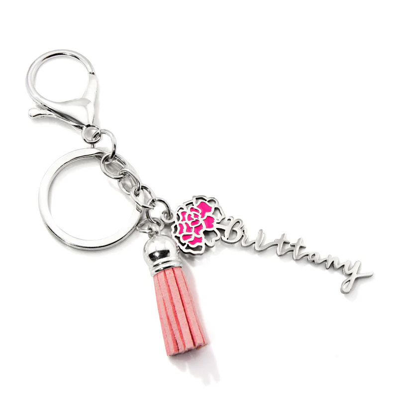 A silver keychain features a lobster clasp, a circular ring, a pink tassel, and a charm with a name alongside a pink floral design.