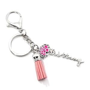 A silver keychain features a lobster clasp, a circular ring, a pink tassel, and a charm with a name alongside a pink floral design.