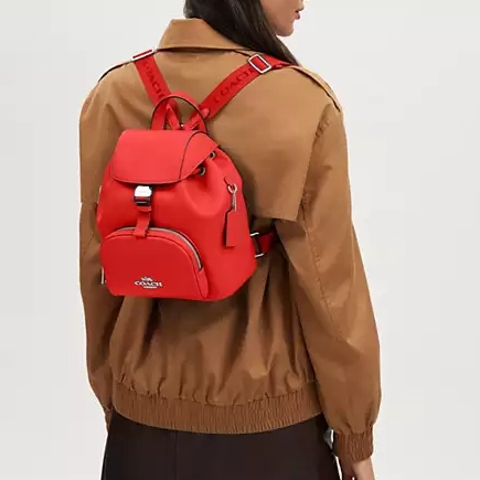 A person wearing a tan jacket with a red backpack.