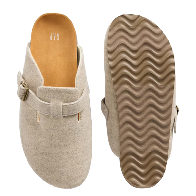 Tan slip-on clogs with a buckle detail, featuring a soft upper fabric and a wavy-patterned rubber sole for grip.