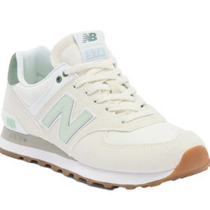 A light beige New Balance 574 sneaker with mint green accents and a gum sole, featuring the iconic \“N\“ logo and \“574\“ branding on the tongue.