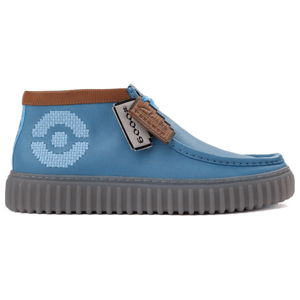 Blue high-top sneaker with a brown accent, featuring a circular pixelated design on the side and a ribbed gray sole, accompanied by decorative tags.