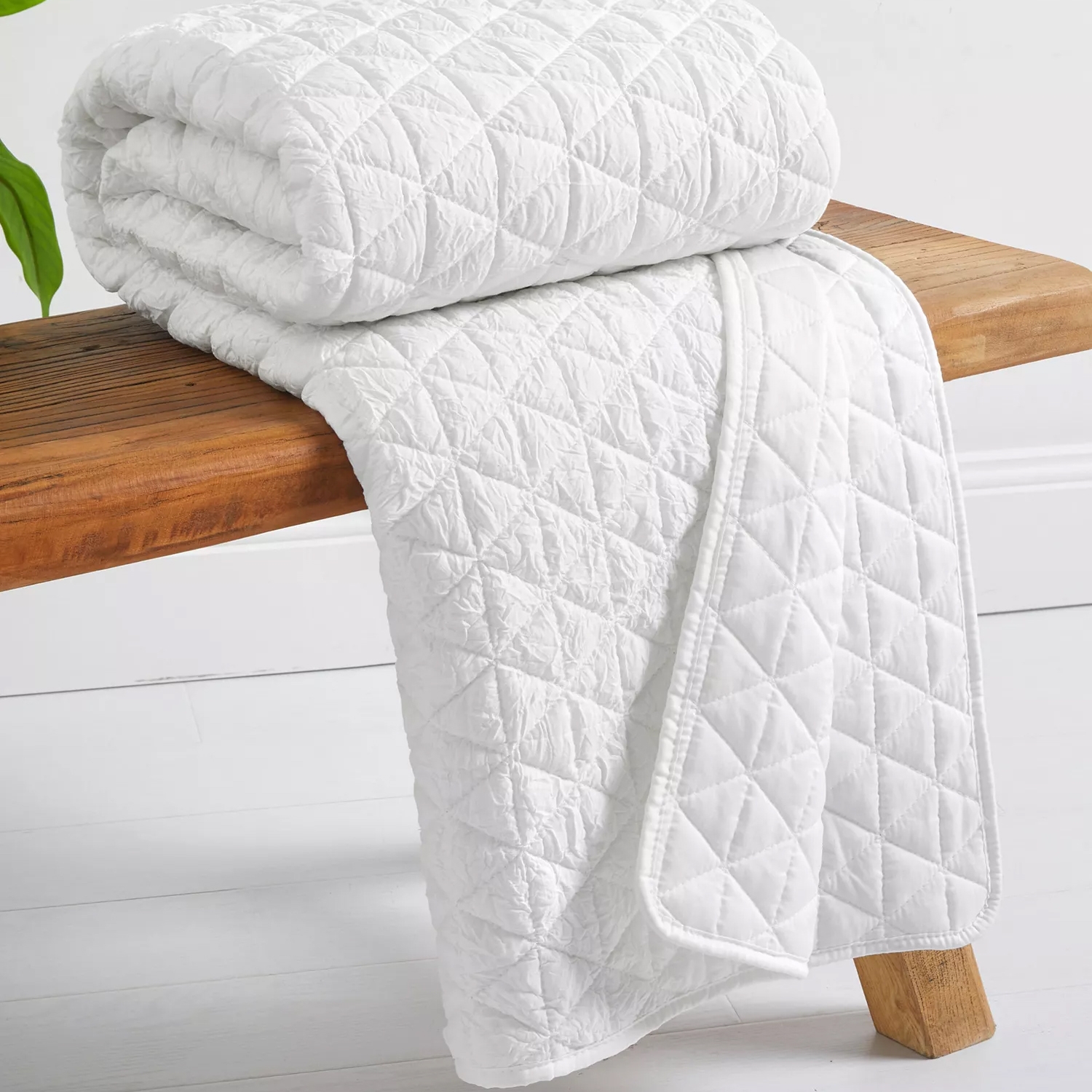 A white, quilted blanket with a diamond pattern is neatly folded and draped over a wooden bench.