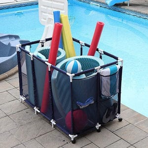 A portable storage bin for pool accessories is shown by a poolside, containing pool noodles, floats, balls, and towels. The structure features mesh sides and a PVC frame for easy organization and drainage.