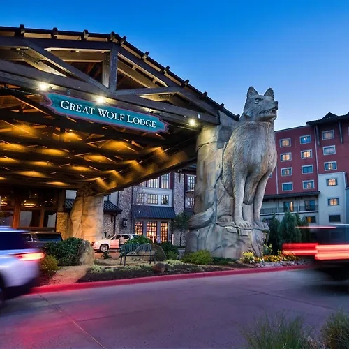 Entrance of Great Wolf Lodge with a large wolf statue overhead and moving vehicles at twilight.