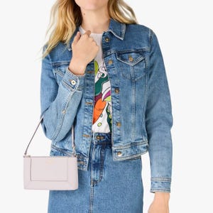 A woman is wearing a denim jacket, a colorful printed t-shirt, and carrying a light pink crossbody purse.