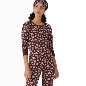 A woman is wearing a burgundy floral-patterned long-sleeve pajama set, accompanied by a matching headband.