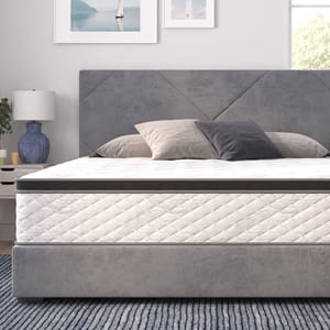 A stylish bedroom setup featuring a modern gray bed with a plush headboard, topped by a white quilted mattress and neutral pillows; complemented by a bedside table, lamp, and framed artwork on the wall.